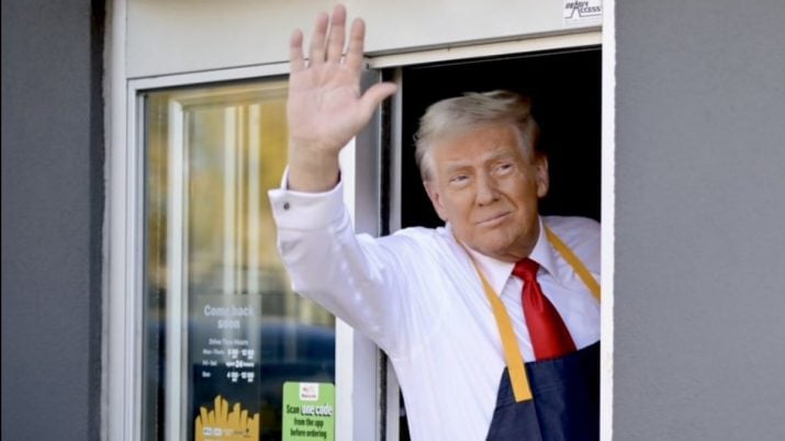 Donald Trump acena para fora de janela do fast food Mc Donald's. Ele usa avental da rede e gravata vermelha.