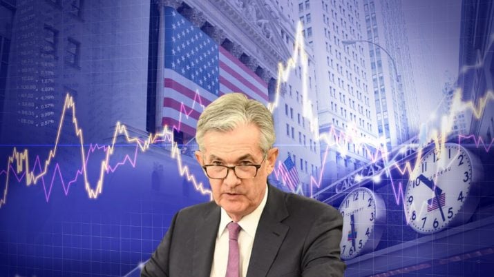 Montagem traz o presidente do Fed, Jerome Powell, em primeiro plano. Ele usa óculos e veste terno cinza escuro com camisa branca. Ao fundo, um cenário com a bolsa de NY e a bandeira dos EUA