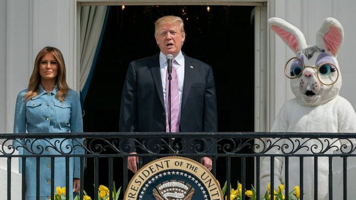 Imagem mostra Melania Trump à esquerda, de traje social azul claro, Donald Trump no centro vestindo terno azul marinho e um coelho da Páscoa à direta.